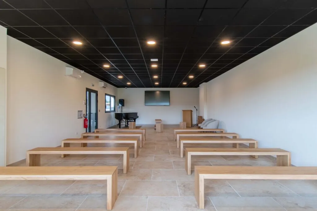 Grande salle d'hommage omniculte avec bancs en bois et piano pour cérémonies funéraires